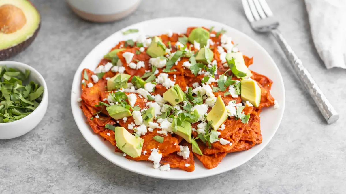 Beyaz tabağın içinde chilaquiles. Sağında çatal var.